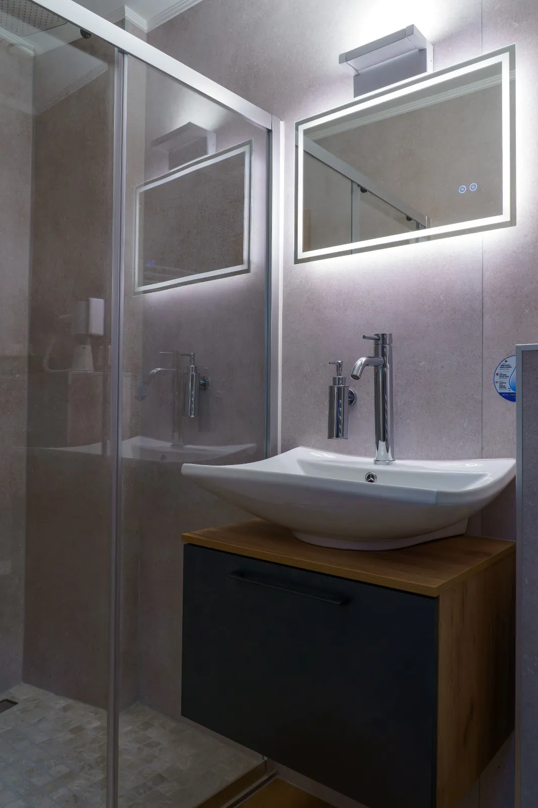 Bathroom with glass shower, basin and lit mirror